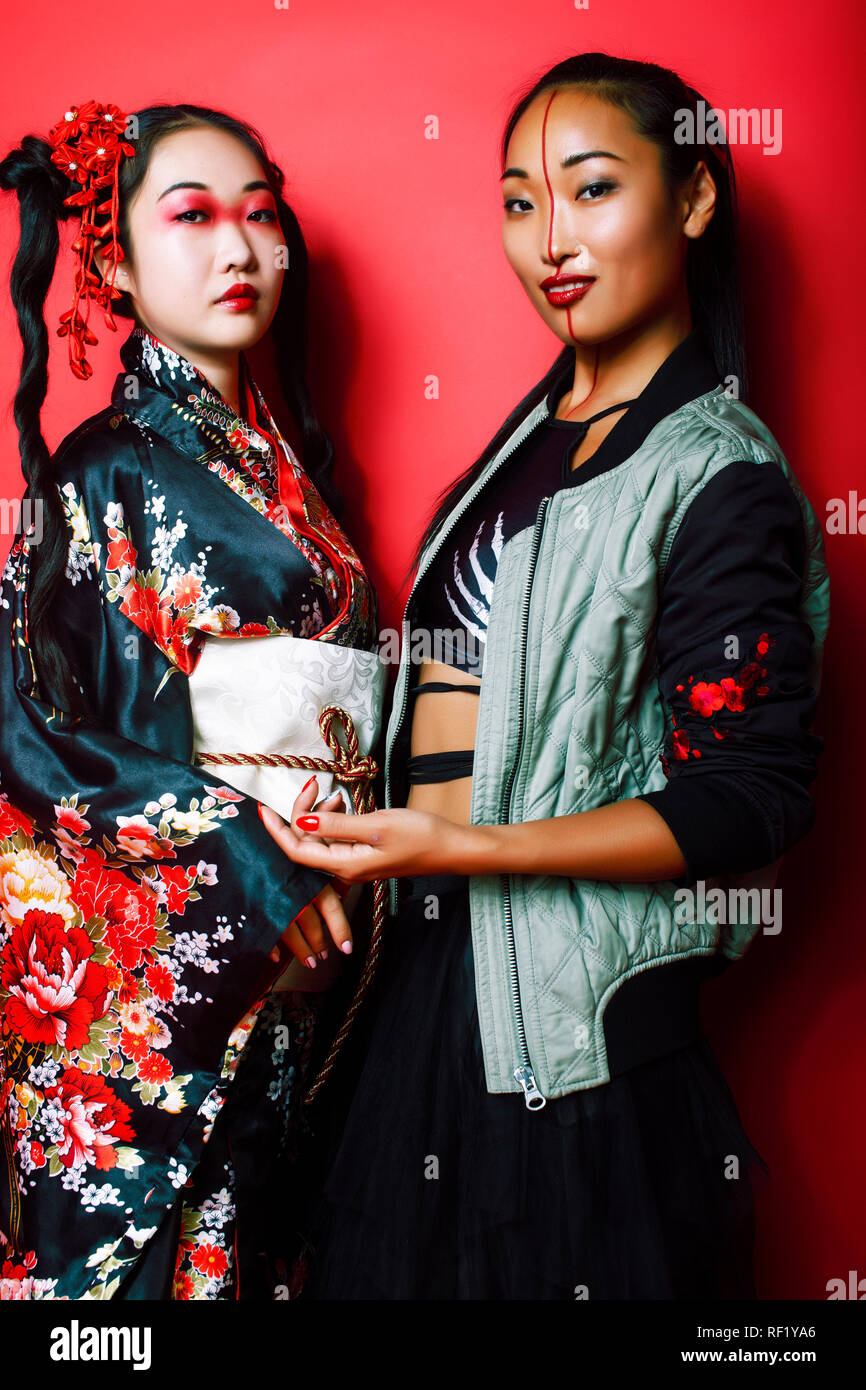 two pretty geisha girls friends: modern asian woman and traditional wearing kimono posing cheerful on red background Stock Photo