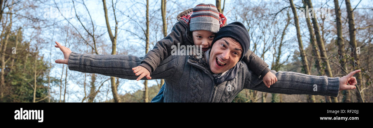 Man giving piggyback ride to happy kid in the forest Stock Photo