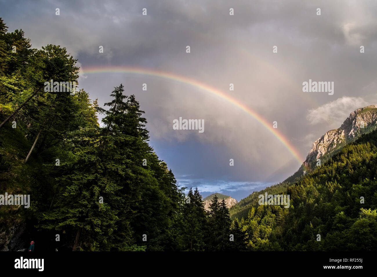 Colorful rainbow between mountains, dark thunderstorm clouds in the distance Stock Photo