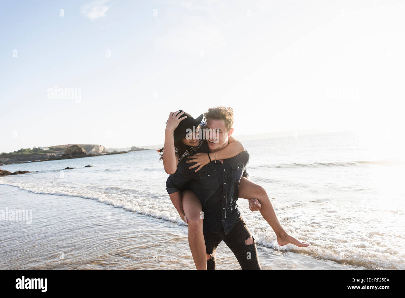 France, Brittany, happy young man carrying girlfriend piggyback at the beach Stock Photo