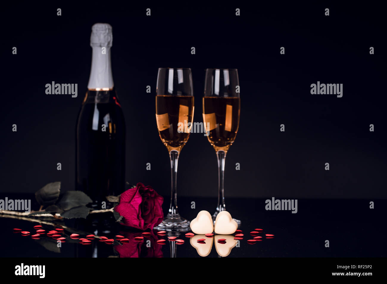 Champagne bottle with two wine glasses and red rose on black background ...