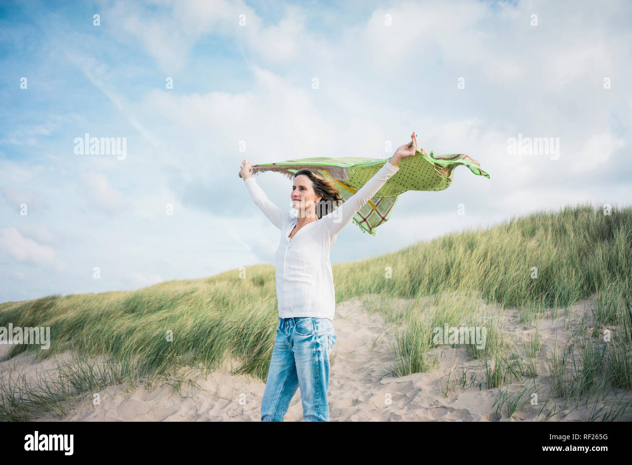 Mature woman holding flapping scarf in the wind, relxiang in the dunes Stock Photo