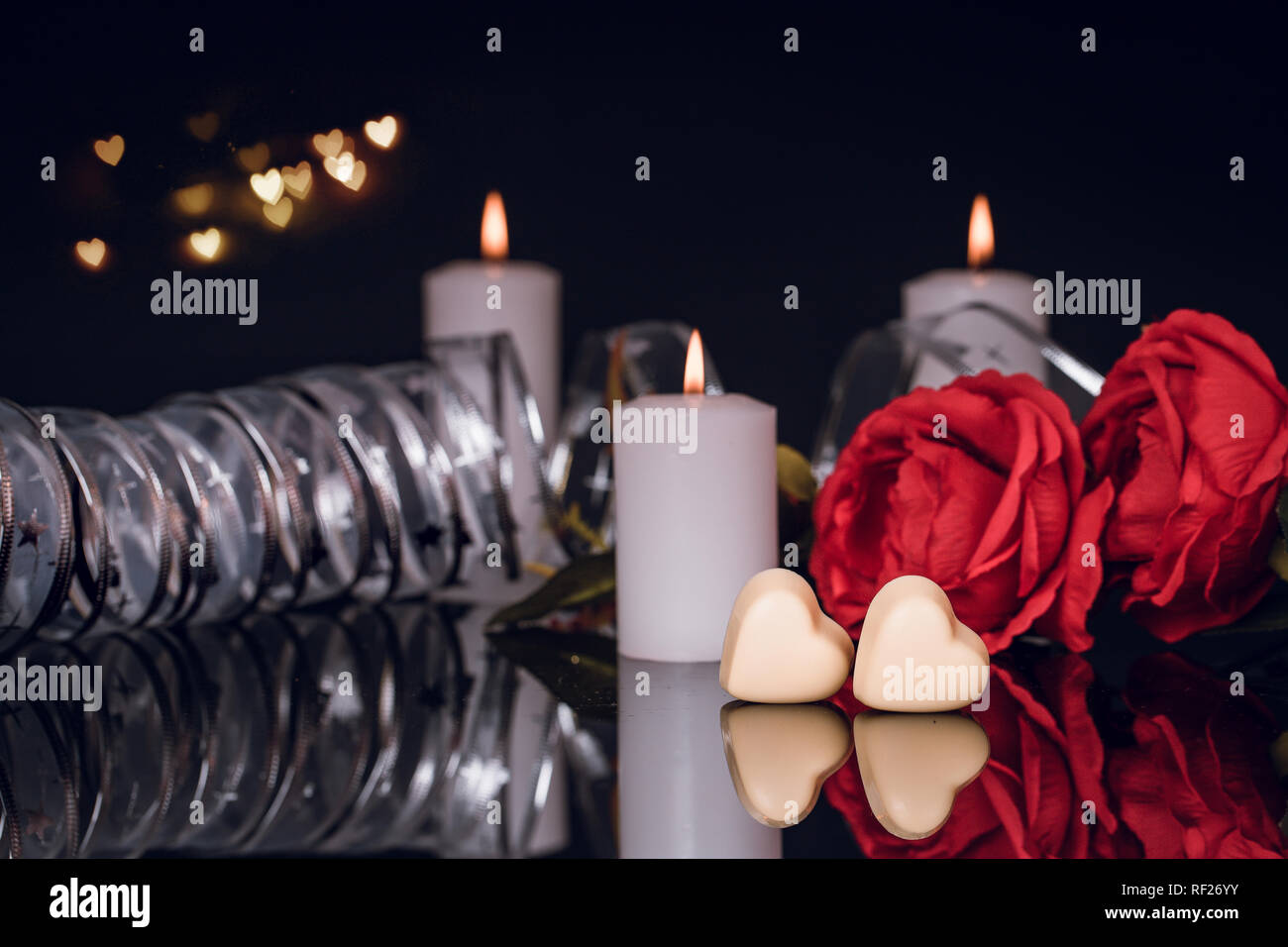 Valentines day greeting card with red roses, candles and heart shaped chocolate on black background. Copy space Stock Photo