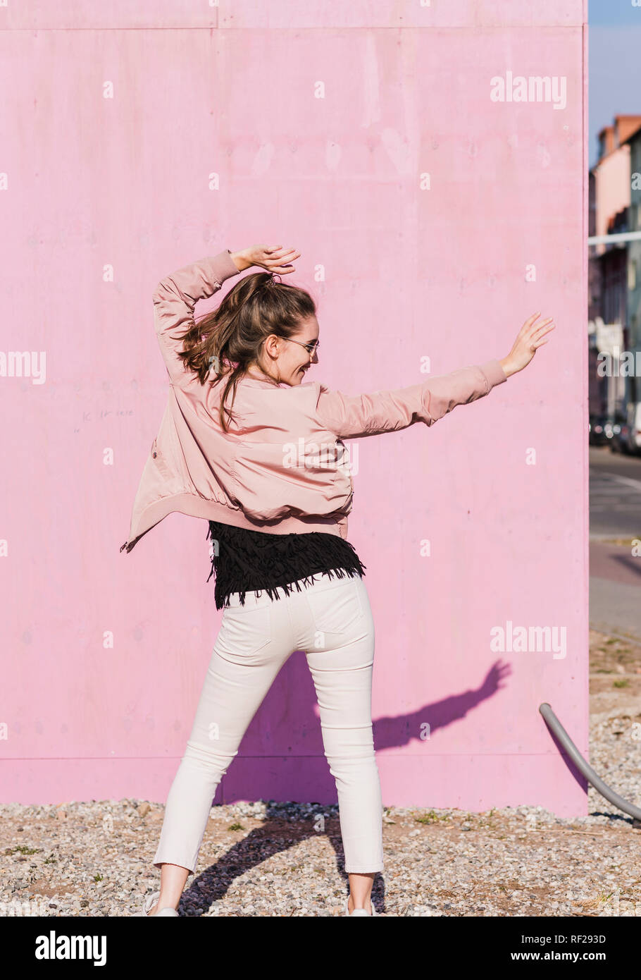 Happy young woman moving in front of pink wall Stock Photo - Alamy