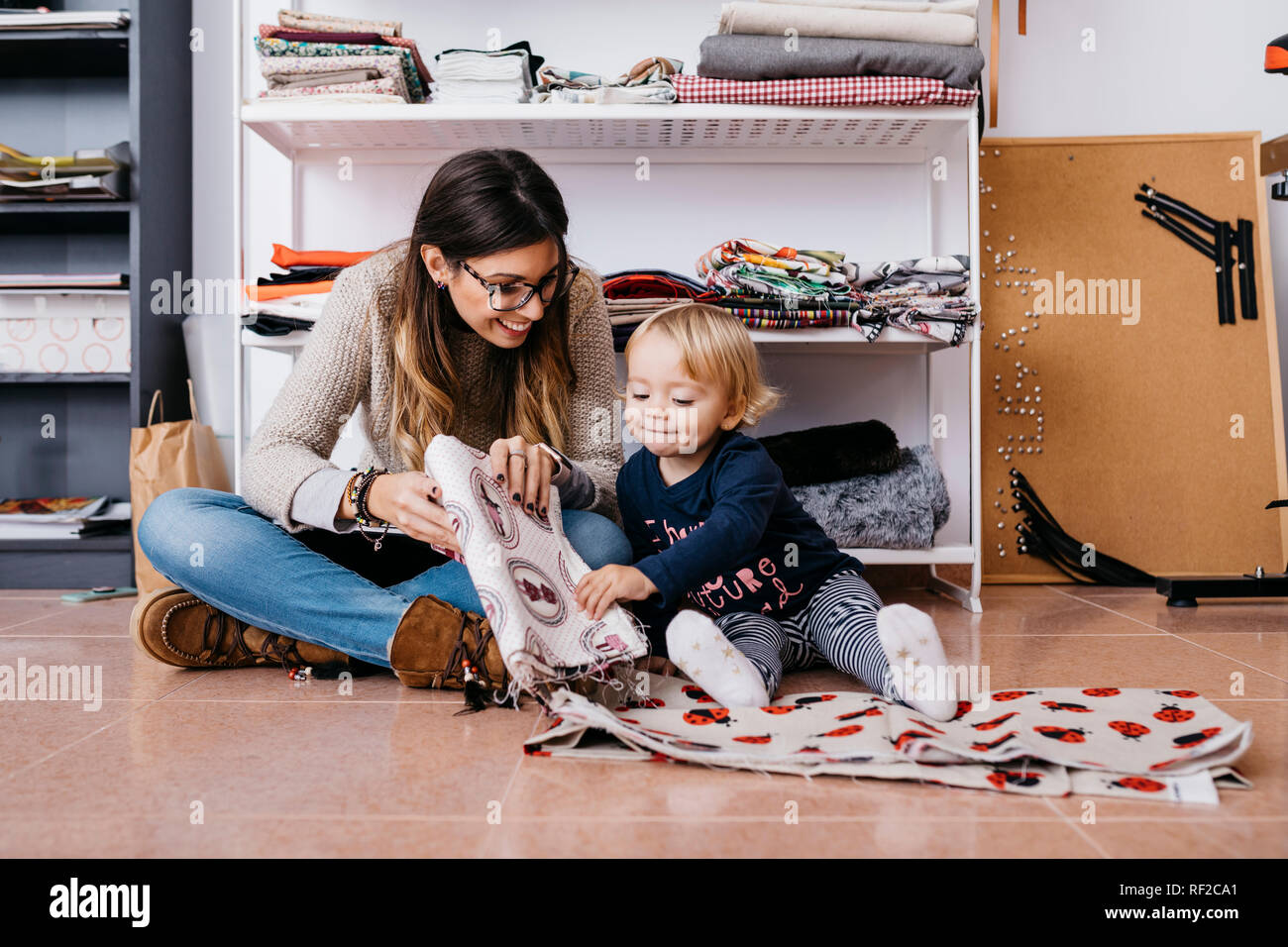 Mother and little daughter sitting on the floor at home checking fabrics Stock Photo