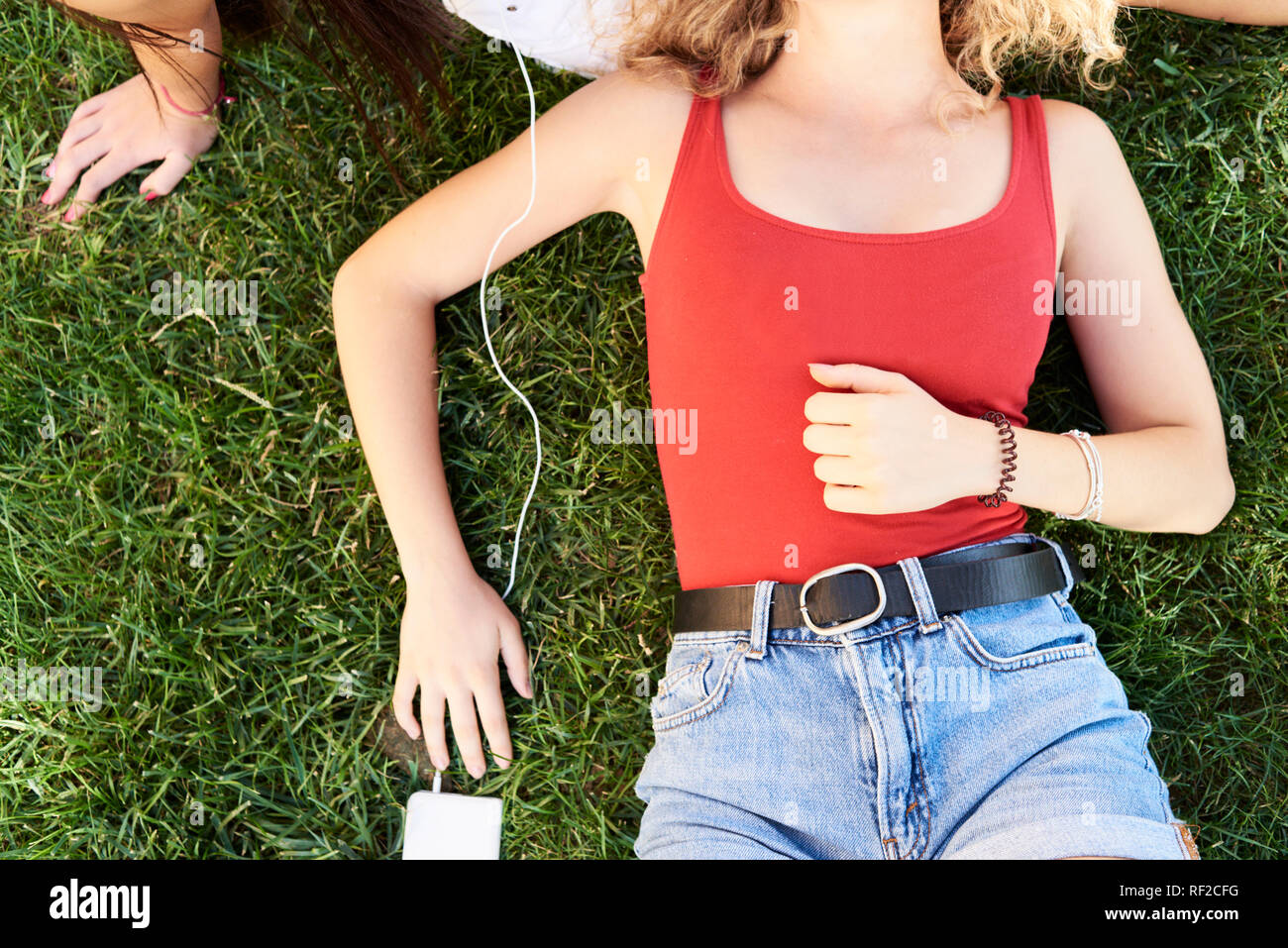 Young woman lying in grass with friend listening to music Stock Photo