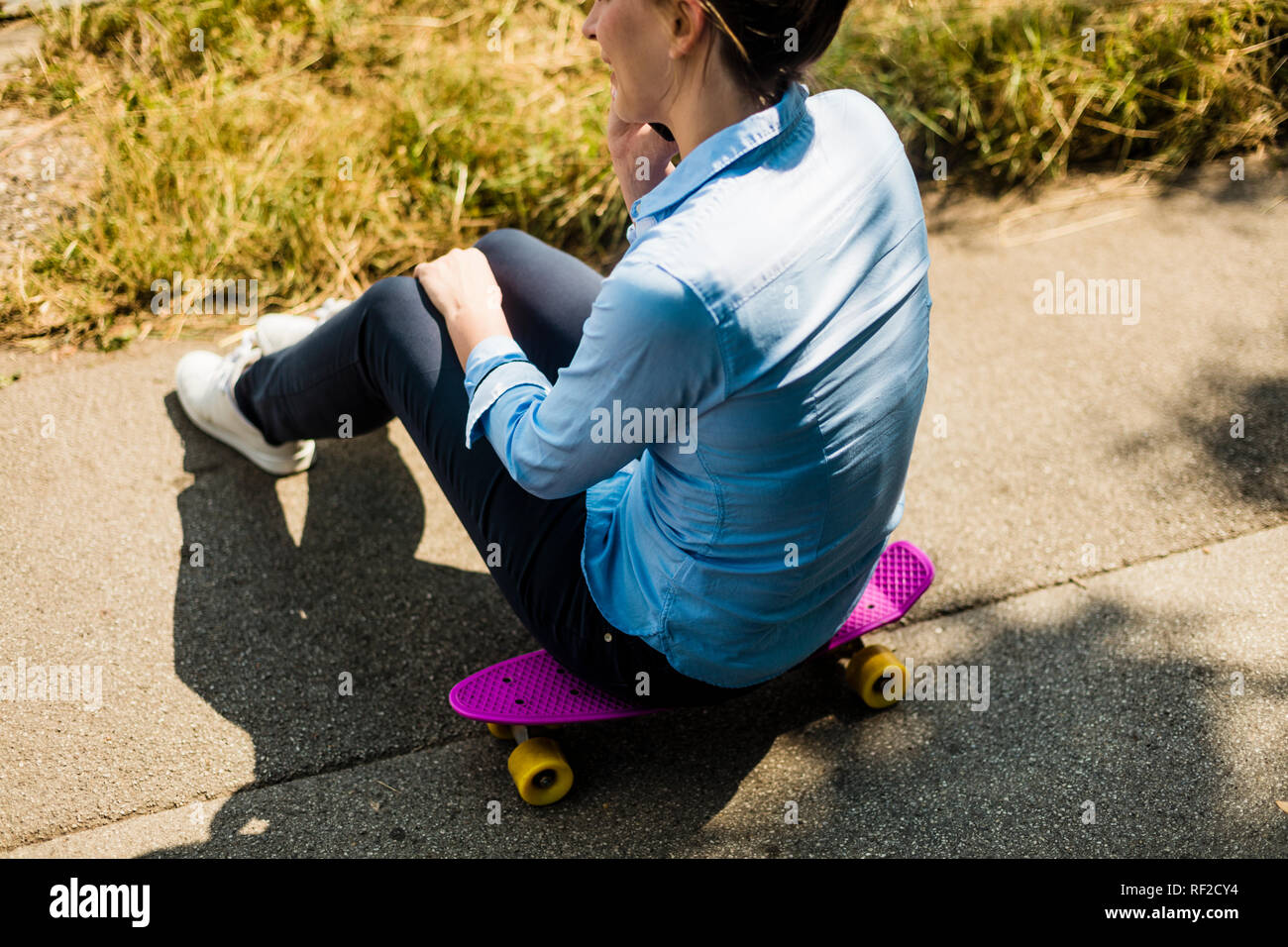 Woman sitting on penny board talking on cell phone Stock Photo