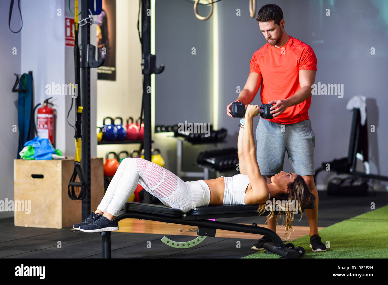 Personal trainer assisting client with weight training, lifting dumbells, lying on bench Stock Photo