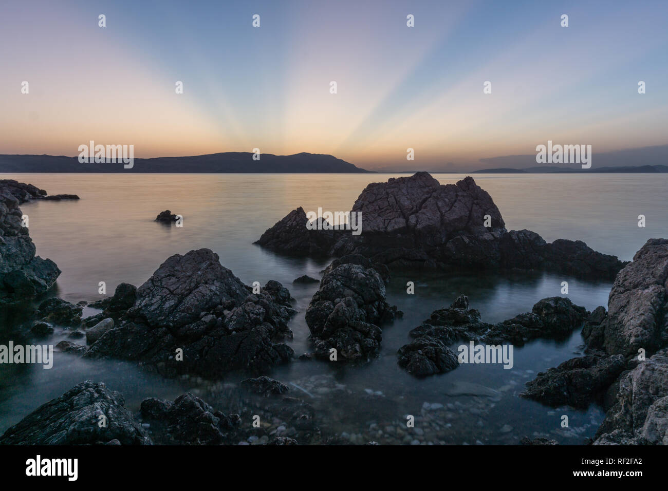 Long exposure photo of water going through rocks on the beautiful sunset, sun going behind island Stock Photo