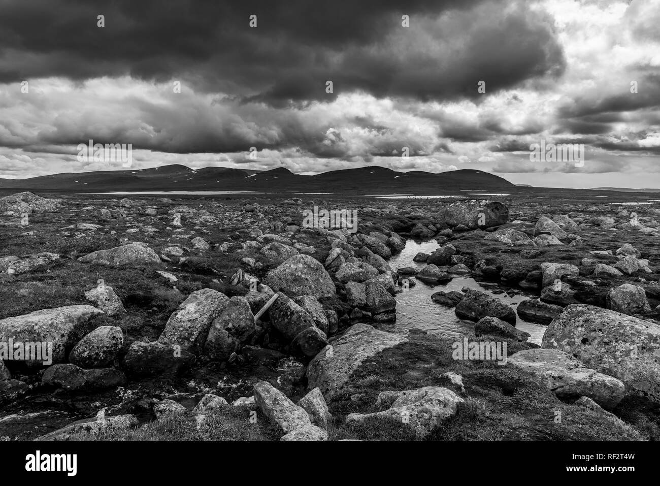 A view of rocky and stone terrain with stormy clouds covered with mountains in the background. Norway, around Beitostolen. Stock Photo