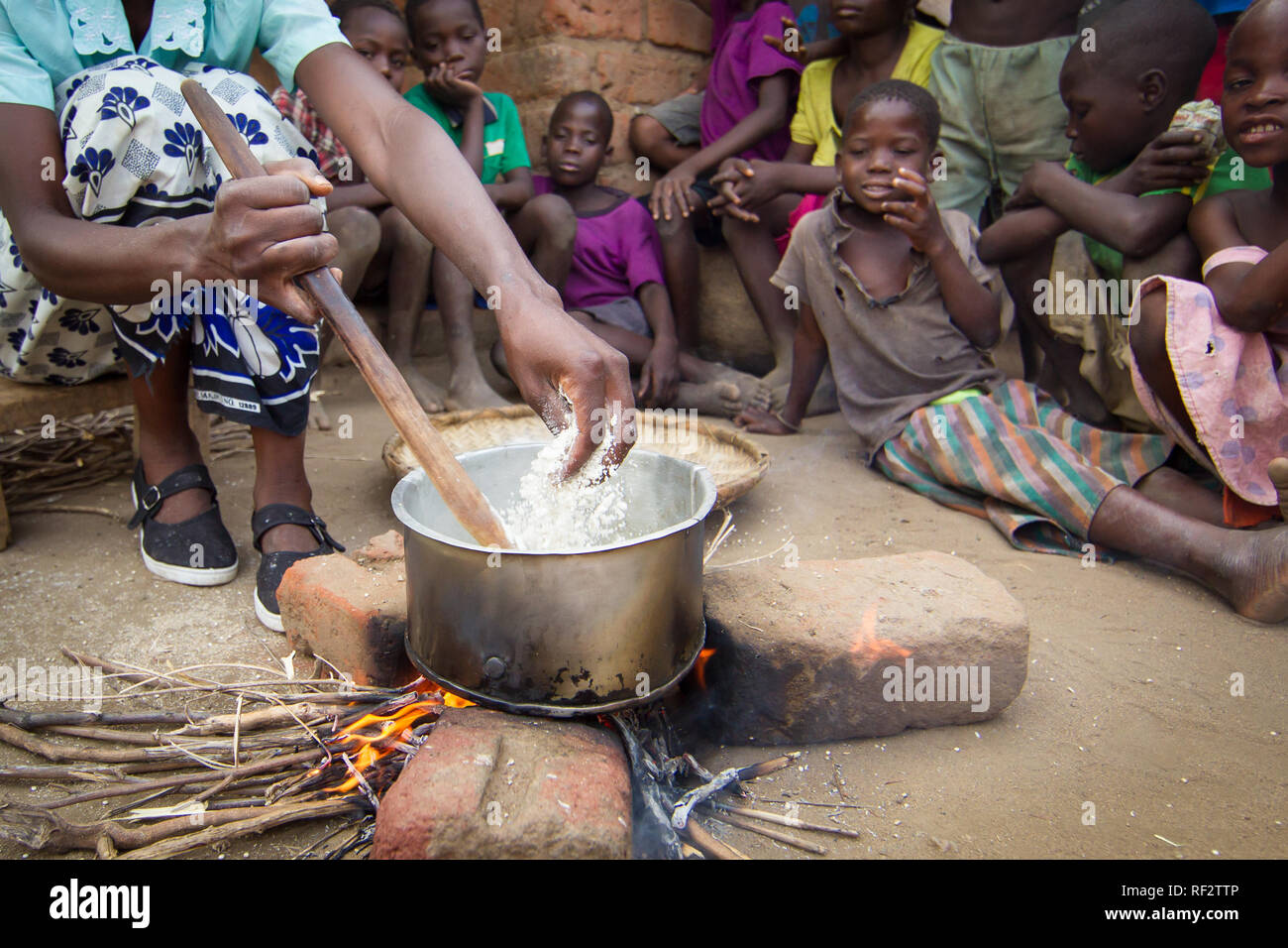 A Malawian woman adds hand-ground sorghum flour to a pot of nsima cooked over an open fire during a visit for tourists to Majete Wildlife Reserve Stock Photo