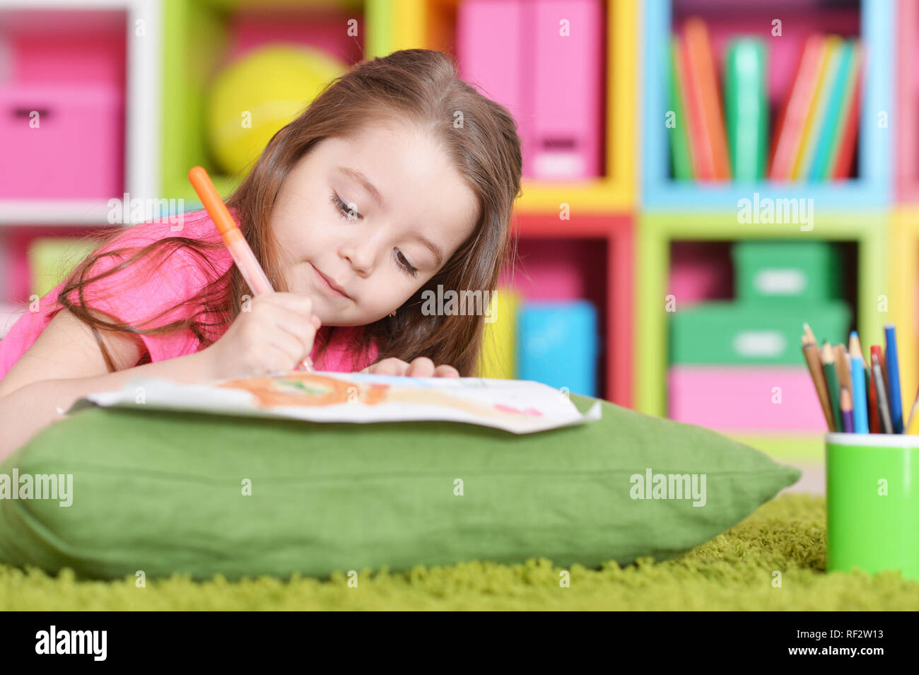 Cute little girl in pink shirt drawing while lying on floor Stock Photo ...