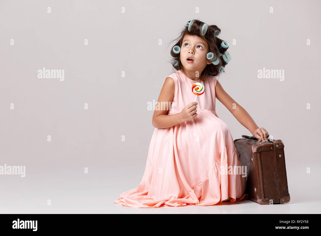 Funny Little Girl In Pink Dress And Hair Curlers Holding