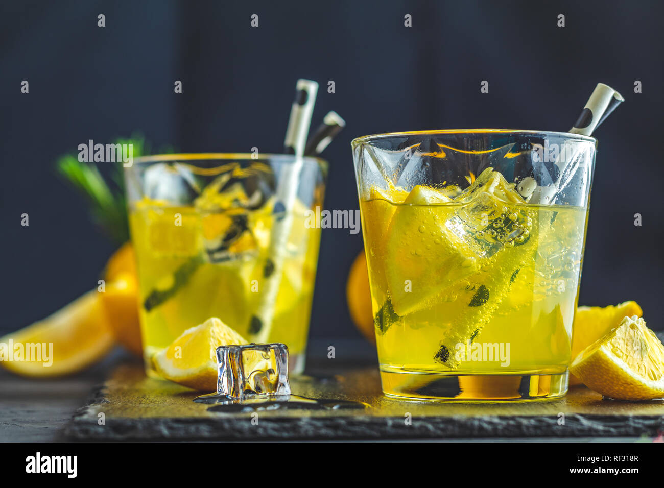 Lemon alcohol drink cocktail with ice, lemon and rosemary herb on black