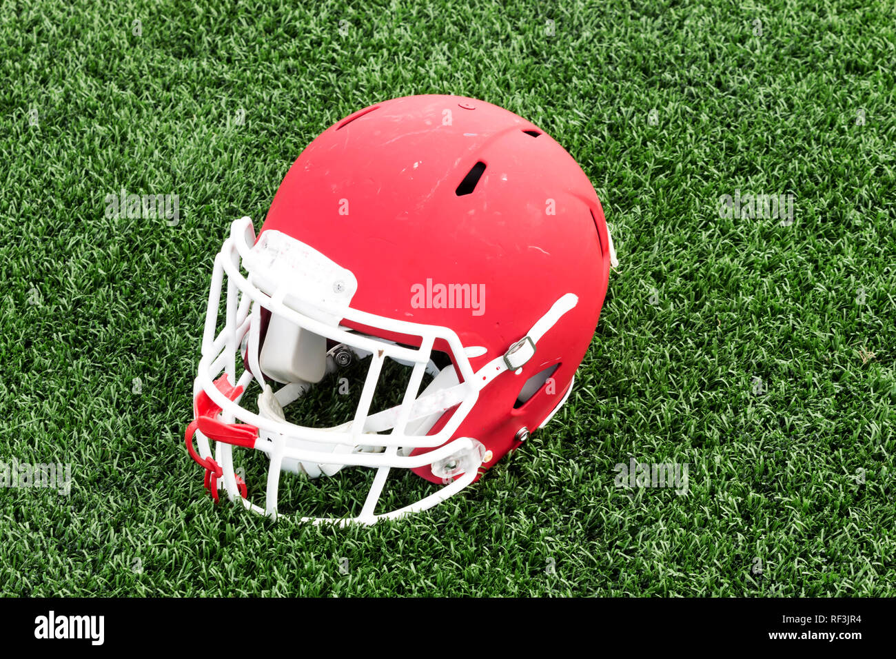 A red football helmet placed on a green turf field with a red
