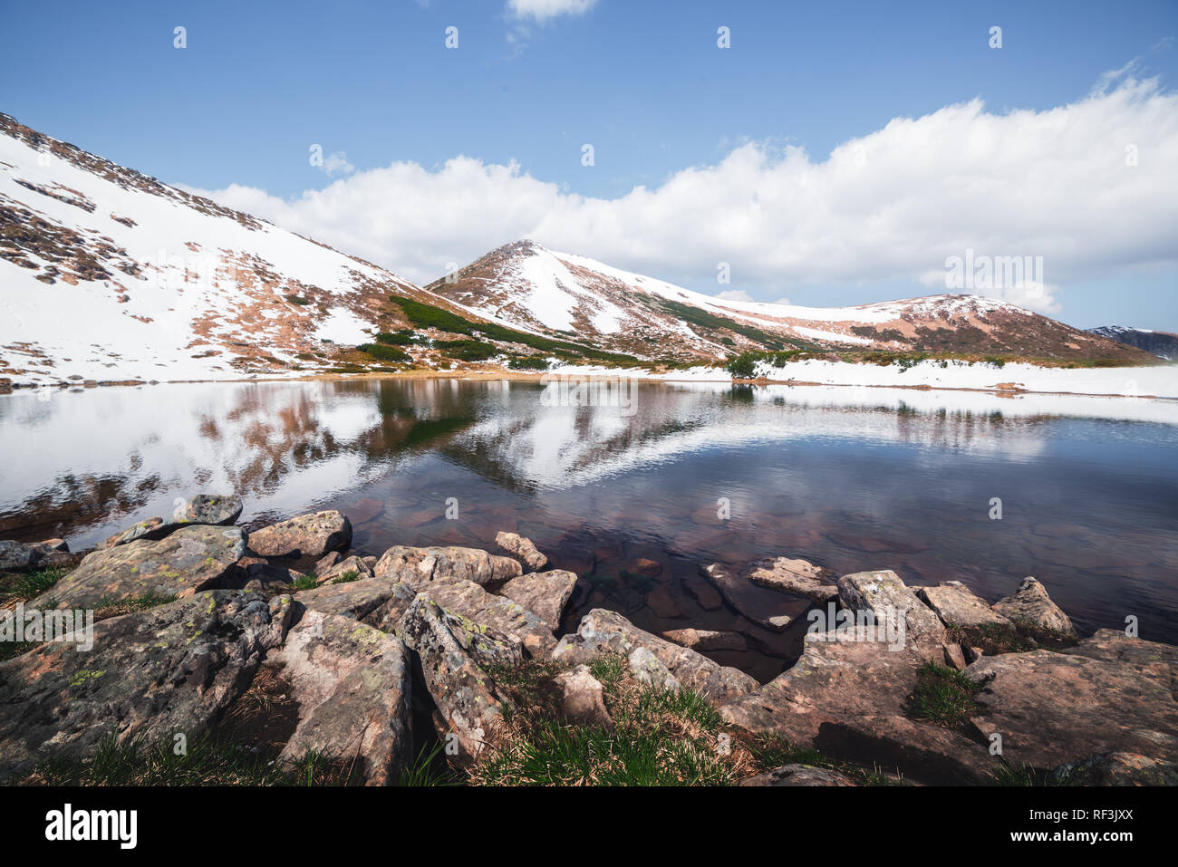 Spring mountain lake with clear water and red stones. Picturesque winter landscape with snowy hills under a blue sky Stock Photo