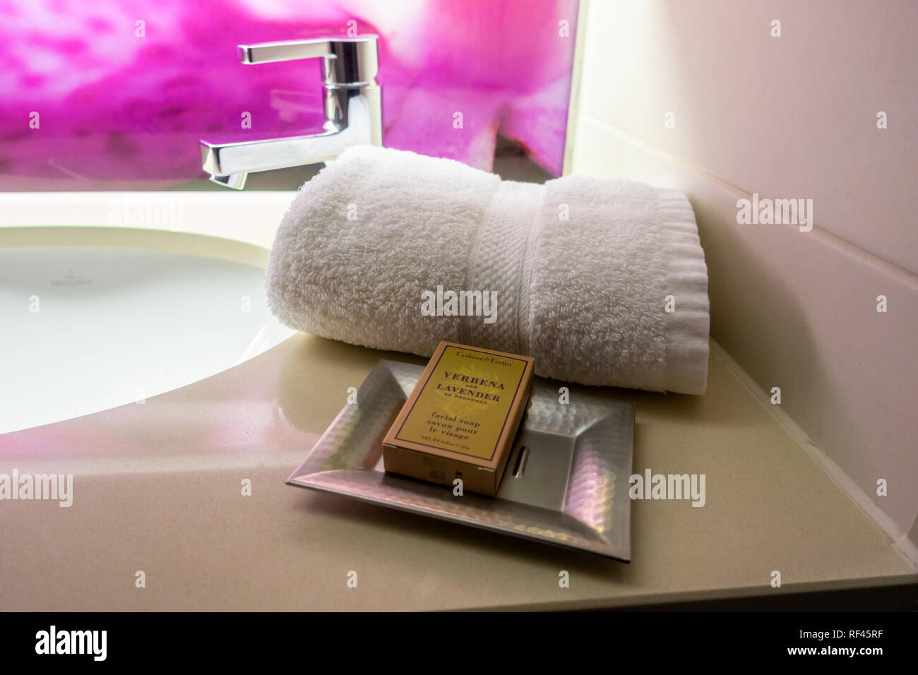 A white towel and packet of soap neatly arranged in a hotel bathroom. Stock Photo