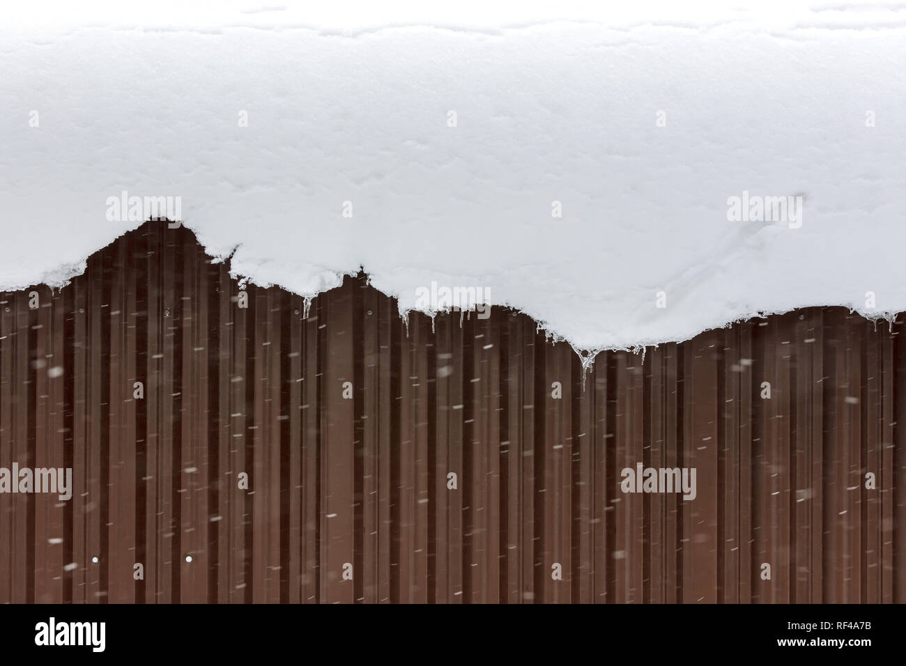much snow hanging from the roof down against corrugated metal wall Stock Photo