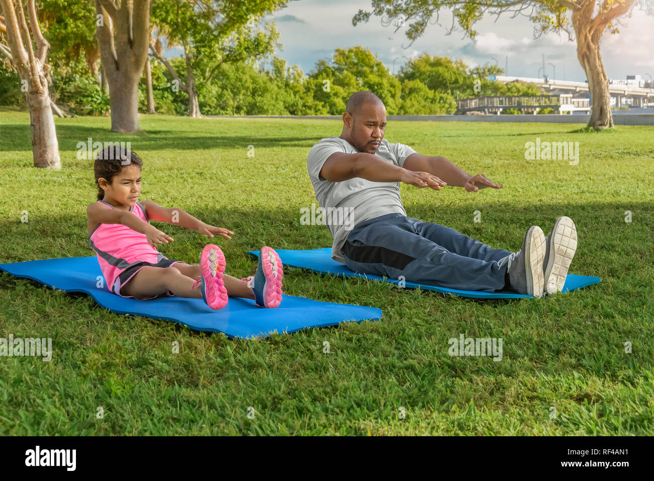 Father and daughter stick together during the morning exercise. The young girl enjoys situps with daddy. Stock Photo