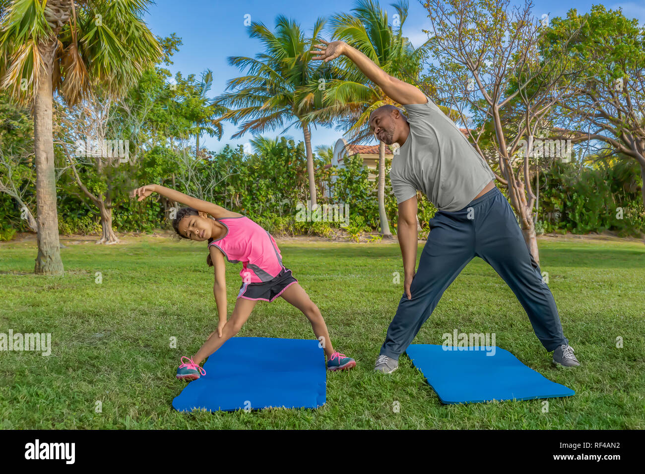 Father and daughter the importance of side stretching as part morning exercise. The little girl struggles to reach as far as daddy. Stock Photo
