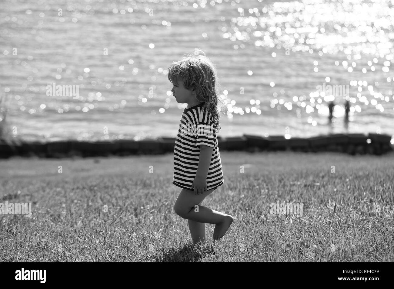 Cute baby boy in striped tshirt walks on green grass Stock Photo