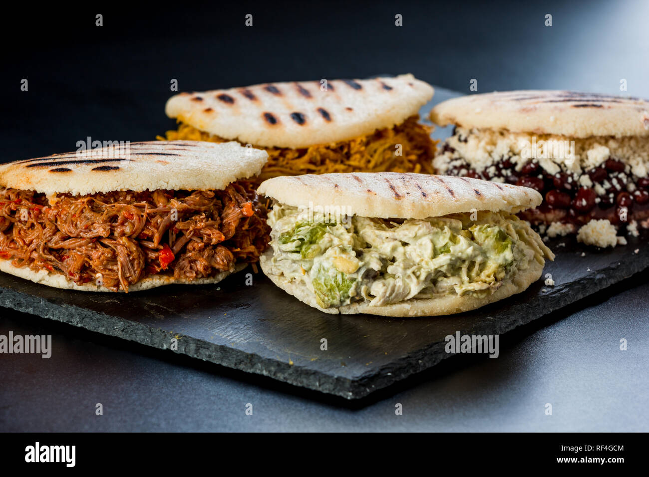 Venezuelan Latin American food, 4 arepas of different stuffing on a black table. Arepa with mechada meat, queen pepeada, black beans with white cheese Stock Photo
