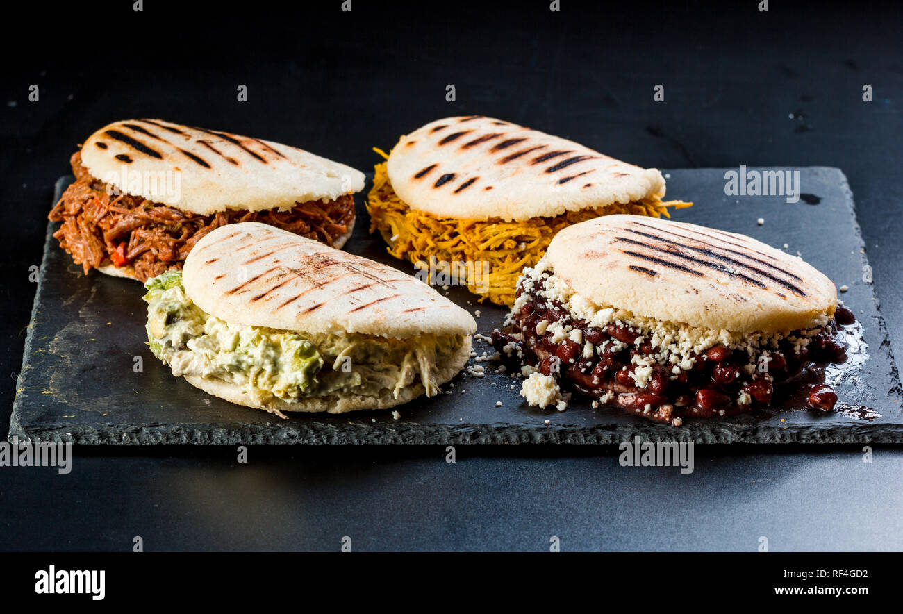 Venezuelan Latin American food, 4 arepas of different stuffing on a black table. Arepa with mechada meat, queen pepeada, black beans with white cheese Stock Photo