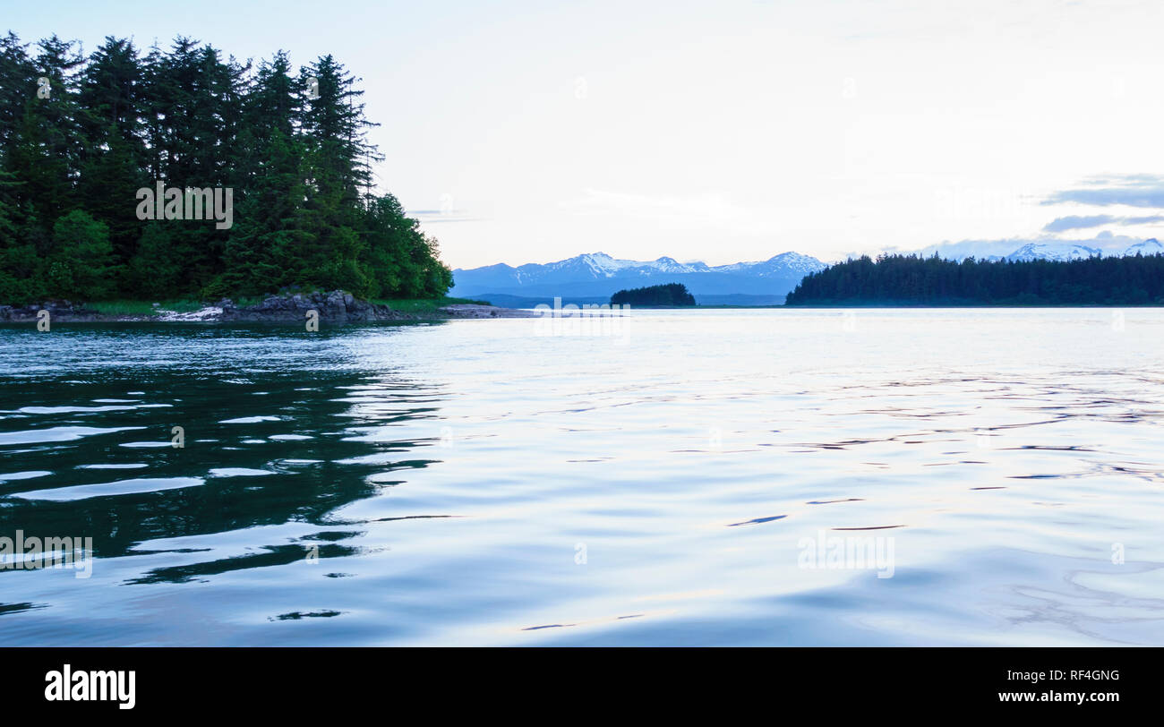 Forested islands, snow-capped mountains and water at twilight in Auke Bay near Juneau, Alaska. Beautiful, peaceful, serene nature scenes. Stock Photo