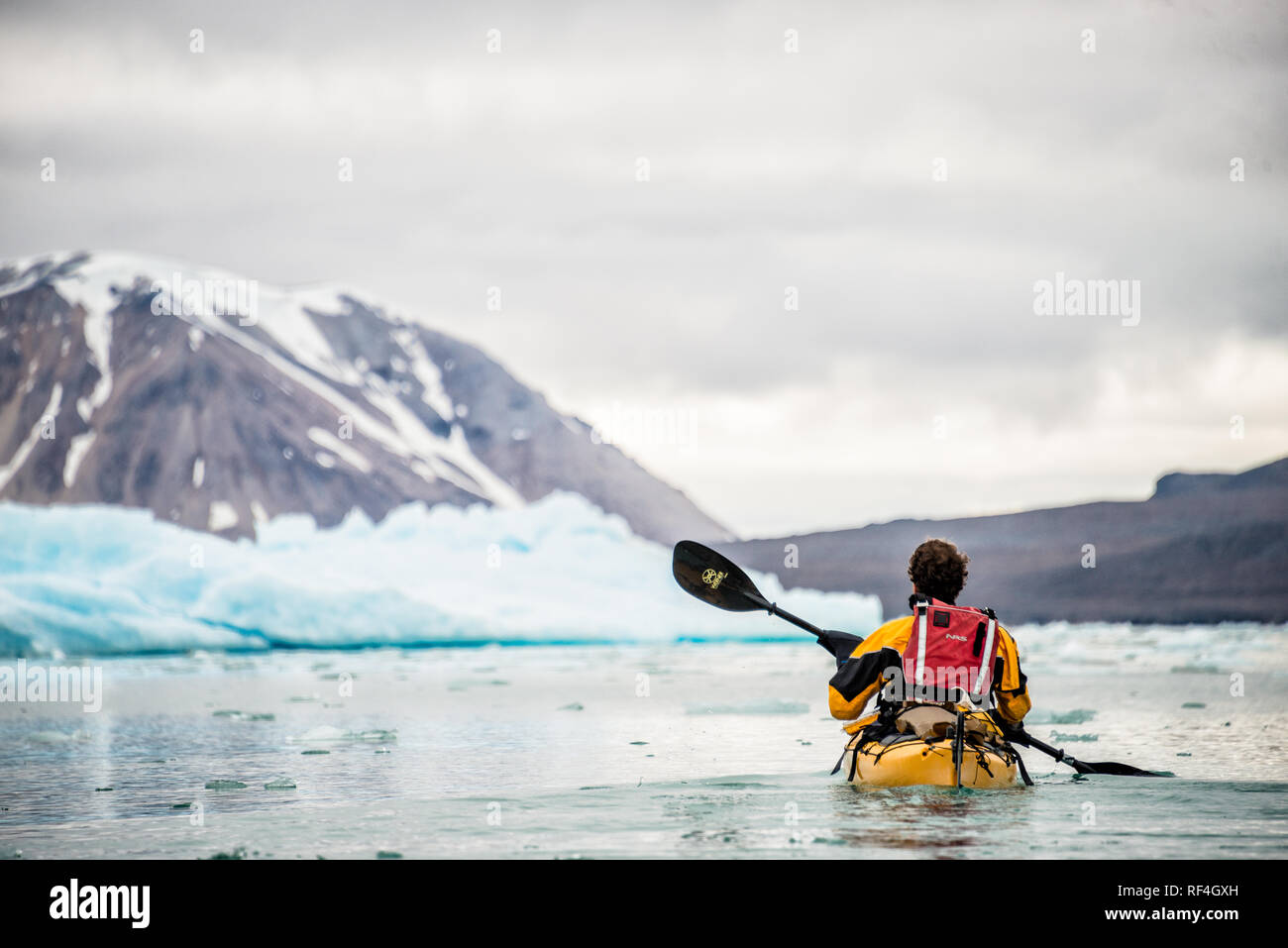 Kayaking Tourist Arctic Landscape Svalbard Norway // SVALBARD, Norway — Kayaking tourists explore the icy waters and pristine landscapes of the Arctic region surrounding Svalbard. This unique and adventurous form of tourism offers an up-close experience with the Arctic environment, showcasing the region's breathtaking beauty and fragile ecosystems. Stock Photo
