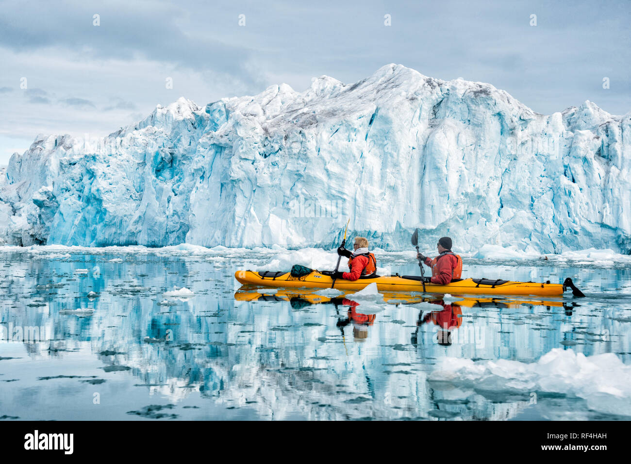 NORDEAUSTLANDET, Svalbard — Two kayakers in a yellow kayak paddle through icy waters near the Bråsvellbreen glacier. The Bråsvellbreen glacier is a significant glacial feature within the Svalbard archipelago, located on the northeastern part of Nordaustlandet island. Kayaking offers visitors an immersive experience in the Arctic environment, providing close views of the glacier's imposing ice formations and the surrounding frigid waters. This activity highlights the stark, natural beauty of the polar region. Svalbard is an archipelago situated in the Arctic Ocean, midway between mainland Norwa Stock Photo