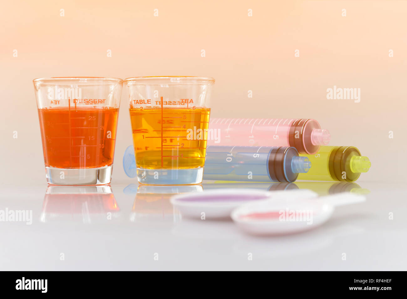 Medicinal cup, oral syringe and teaspoon filled with oral syrup