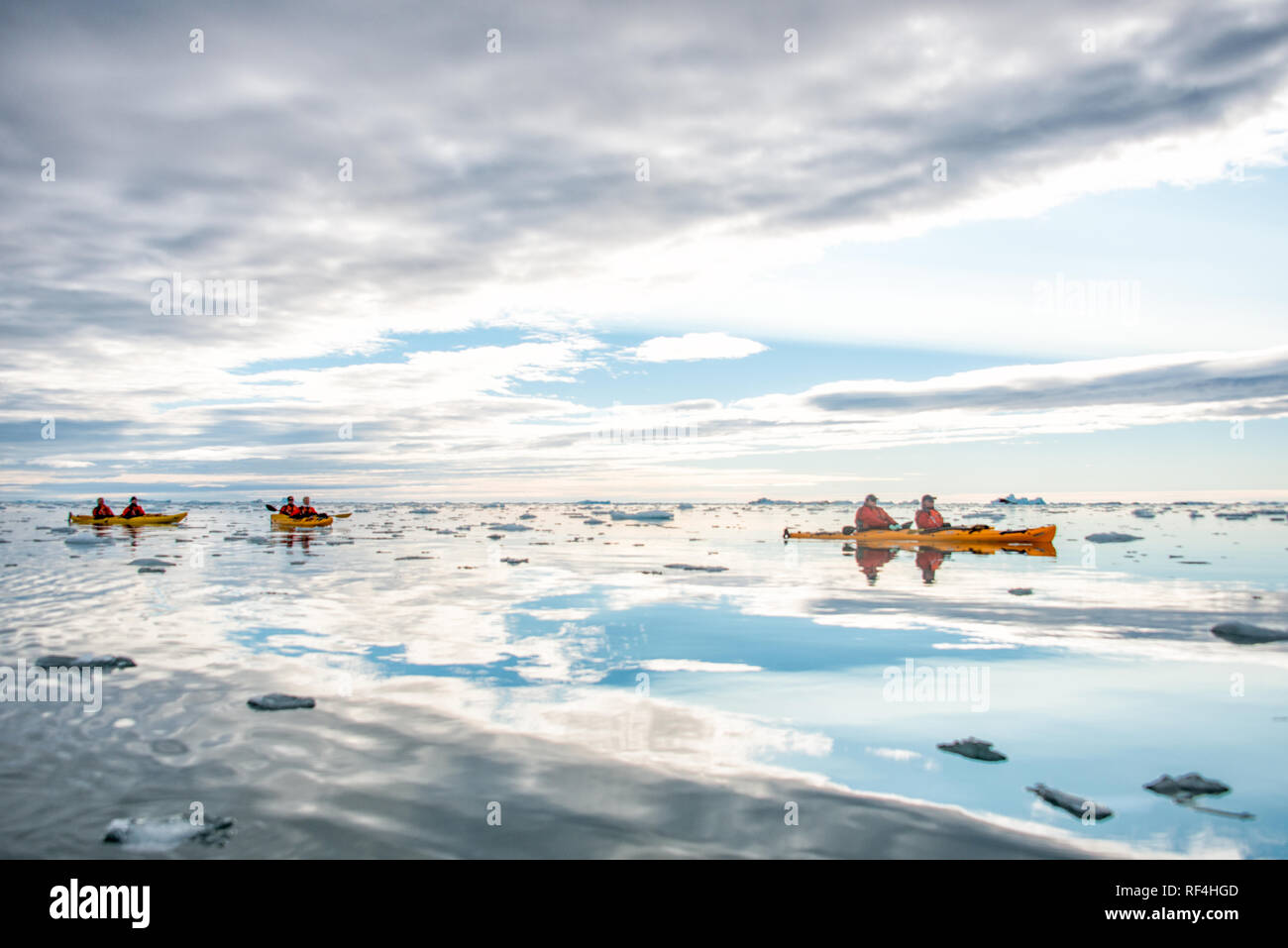NORDEAUSTLANDET, Svalbard — Kayakers paddle through the Arctic waters near the Brasvellbreen glacier, one of the largest ice caps in Svalbard. This remote region of Norway is known for its dramatic glacial landscapes and opportunities for polar exploration. The kayaks navigate a calm sea dotted with ice floes, reflecting the dramatic cloudy sky above. Stock Photo