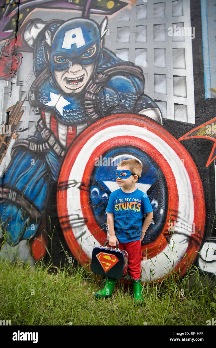 A young boy in an eclectic superhero costume leans against Captain America in a street art mural in Pilsen neighborhood of Chicago Illinois Stock Photo