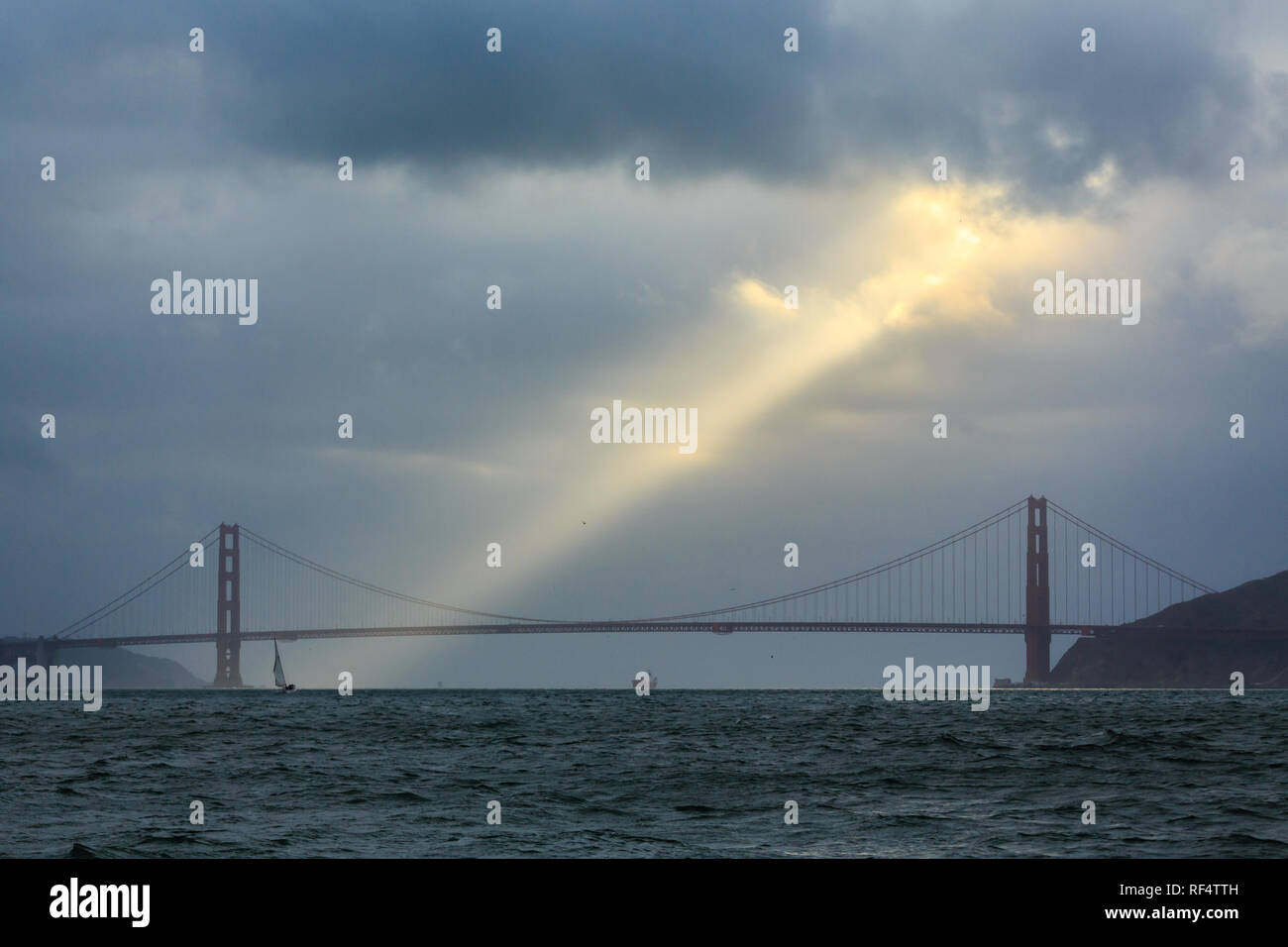 Ray of golden sunshine breaks through the rain clouds above Golden Gate Bridge and San Francisco Bay Stock Photo