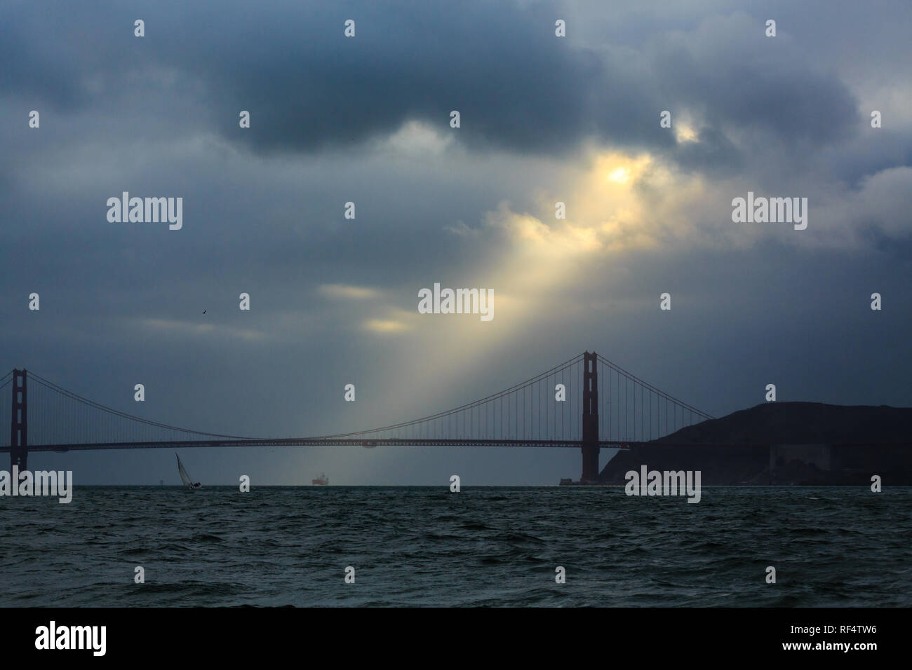 Ray of golden sunshine breaks through the ominous clouds above Golden Gate Bridge and San Francisco Bay Stock Photo