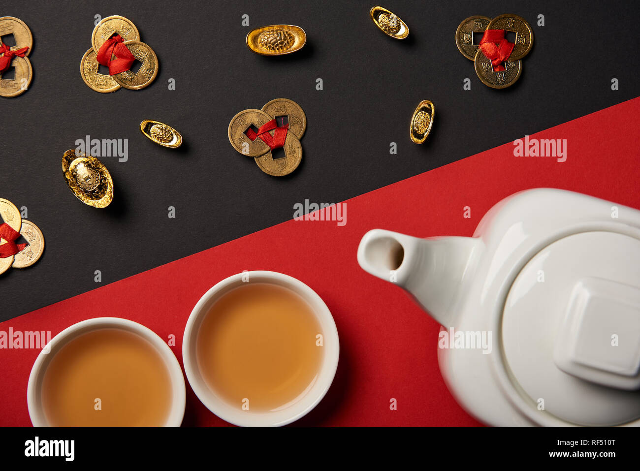 top view of tea pot, cups, gold ingots and feng shui coins on red and black background Stock Photo