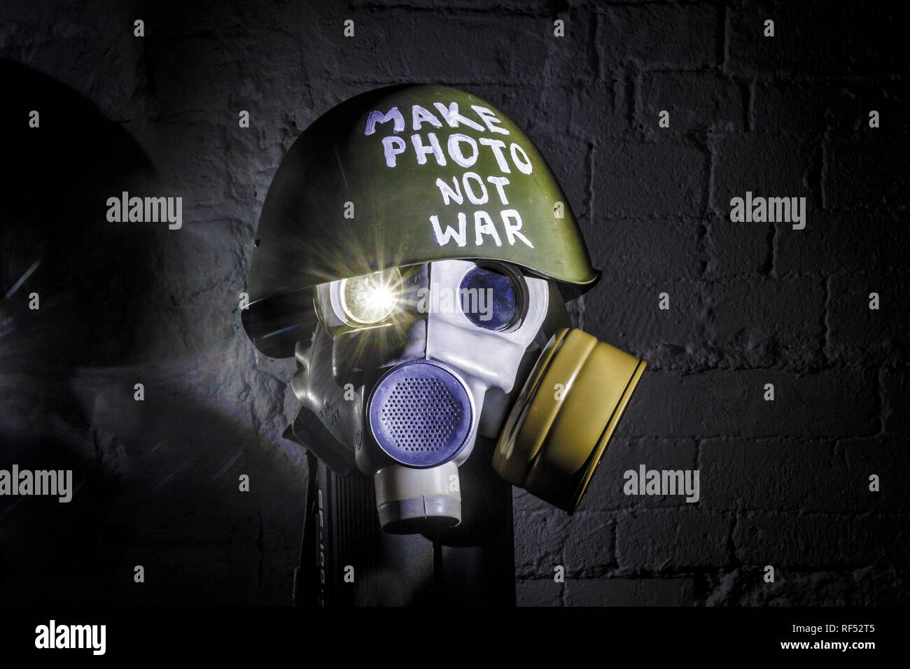 art picture of a military gas mask on a white brick wall with shadows with flash with the inscription make photo not war on Fatherland defender day Stock Photo