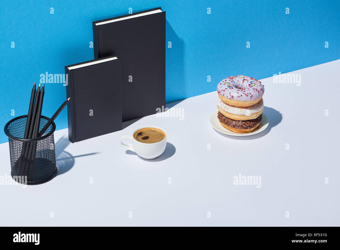 tasty donuts, coffee cup, pencil holder and notebooks on white desk and