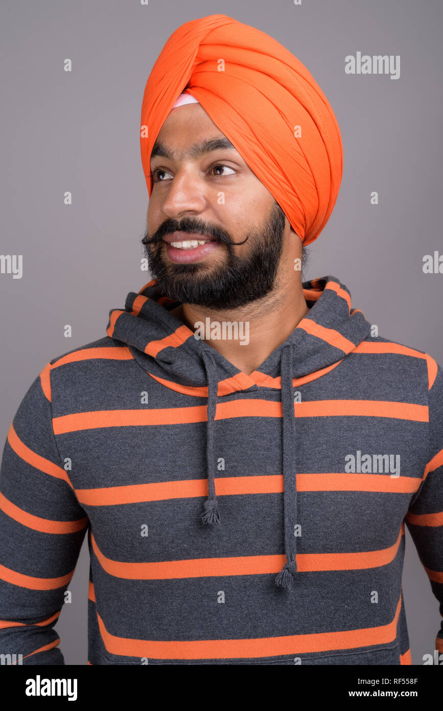 Indian Sikh man wearing orange turban while thinking and smiling Stock Photo