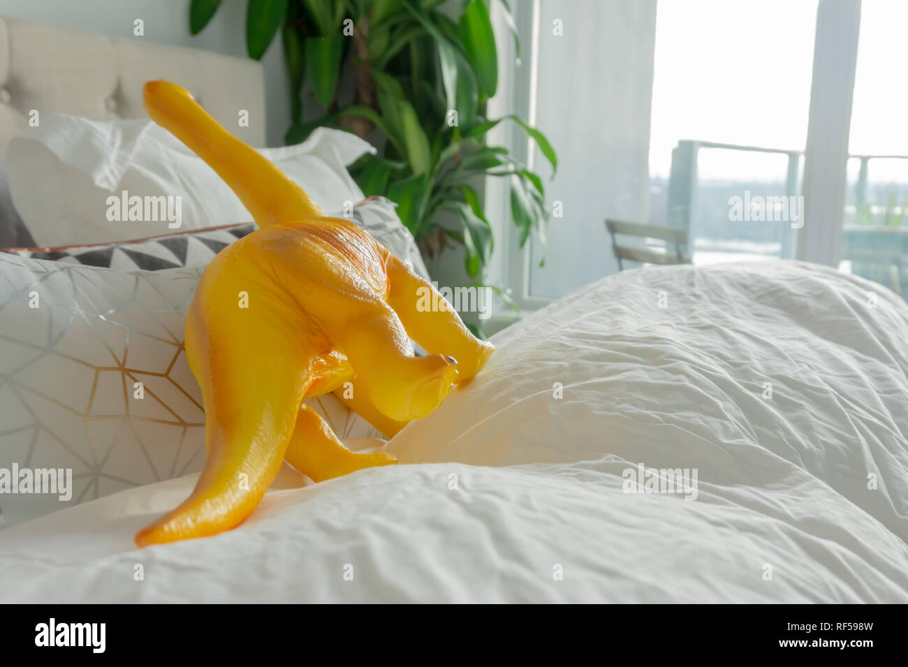 Yellow toy dinosaur in parent bed, depicting parenting lifestyle and a real home. Stock Photo