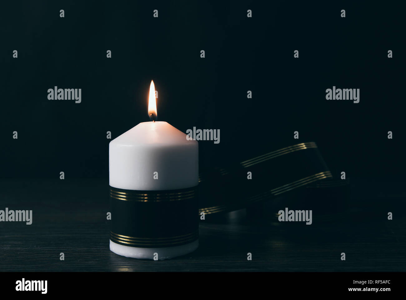 White candle with black ribbon, symbol of remembrance or mourning, black background. Lot of blank copy space for your text. Stock Photo