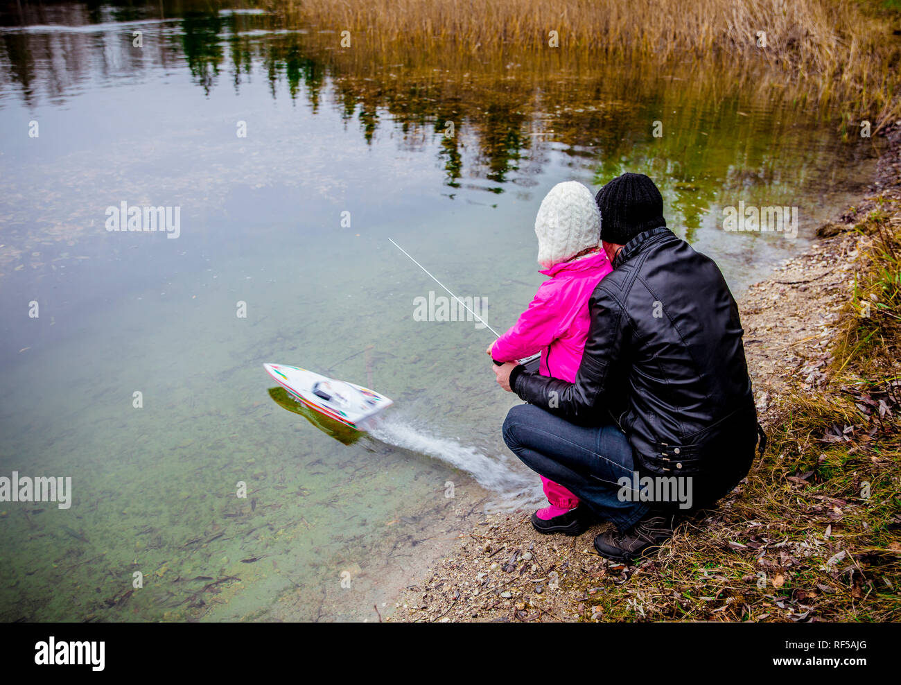Father and daughter are playing together with remote controlled speedboat outdoors in autumn day by the lake in countryside. Stock Photo