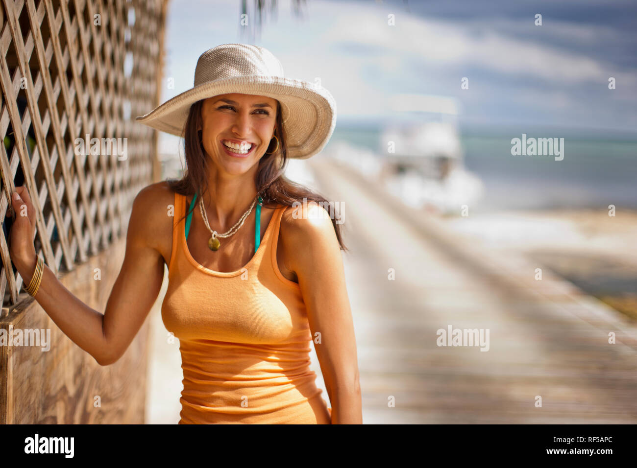 Smiling young woman standing beside a wooden beach hut at a tropical beach. Stock Photo