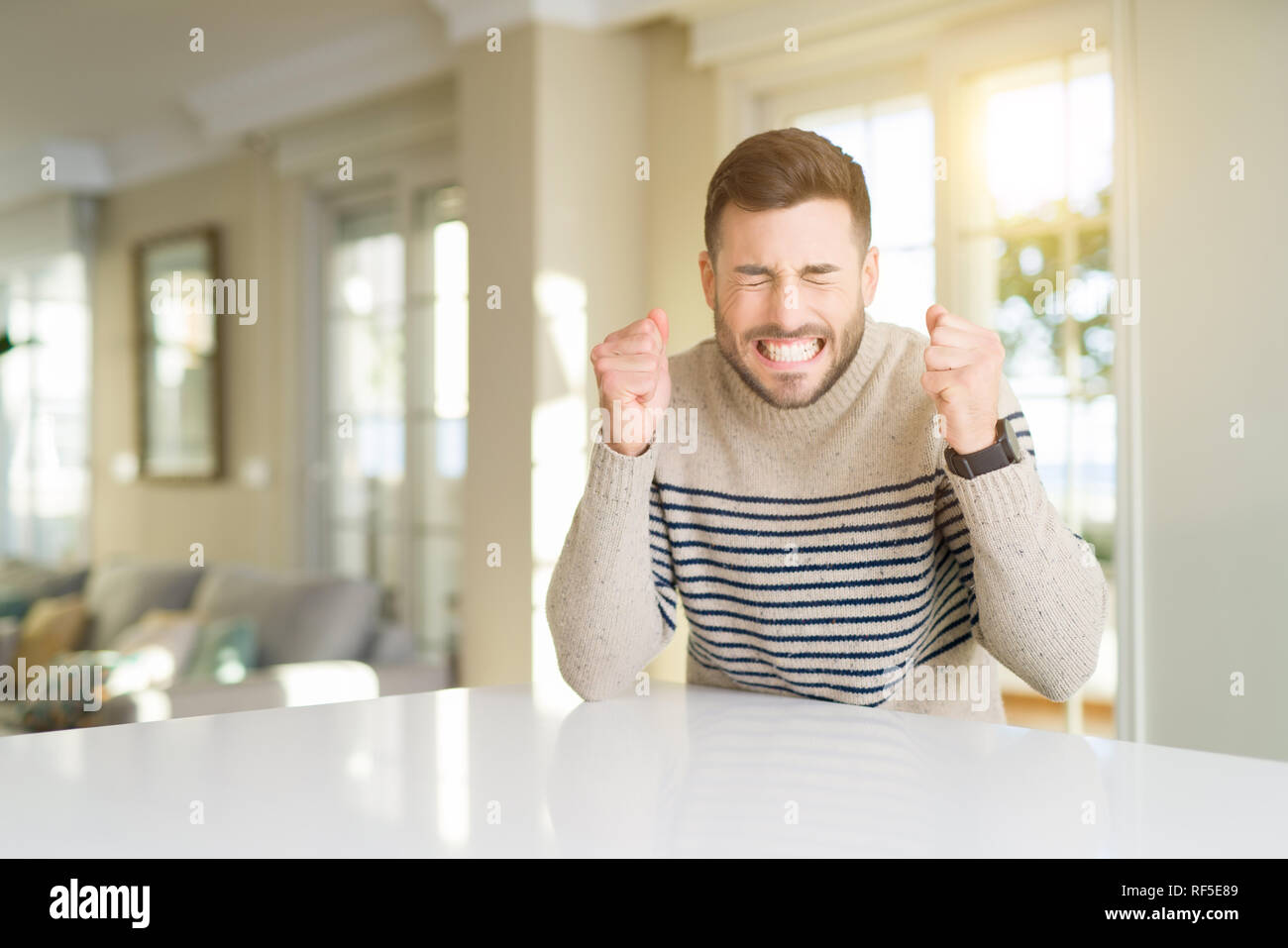 Young handsome man at home excited for success with arms raised ...