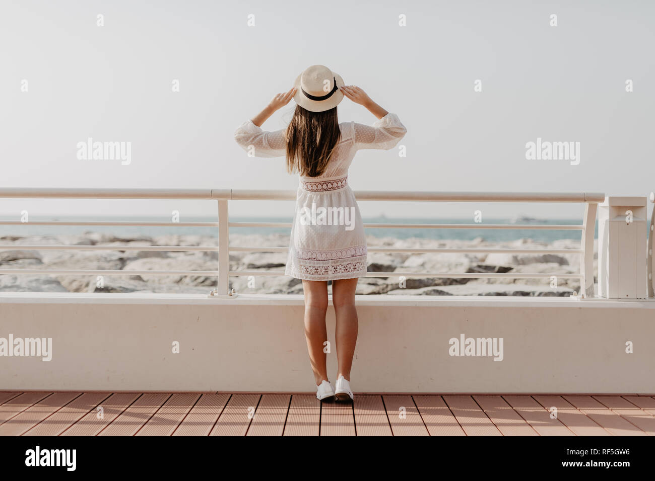 Back view of young woman walking on promenade looking at sea. Summer vacation travel. Stock Photo