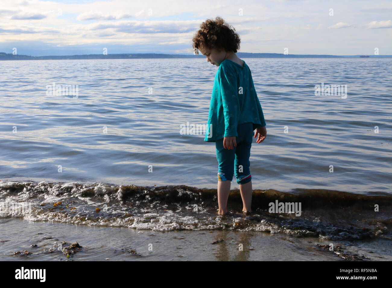 Child wading in the water at the shore of Alki Beach in West Seattle, Washington Stock Photo