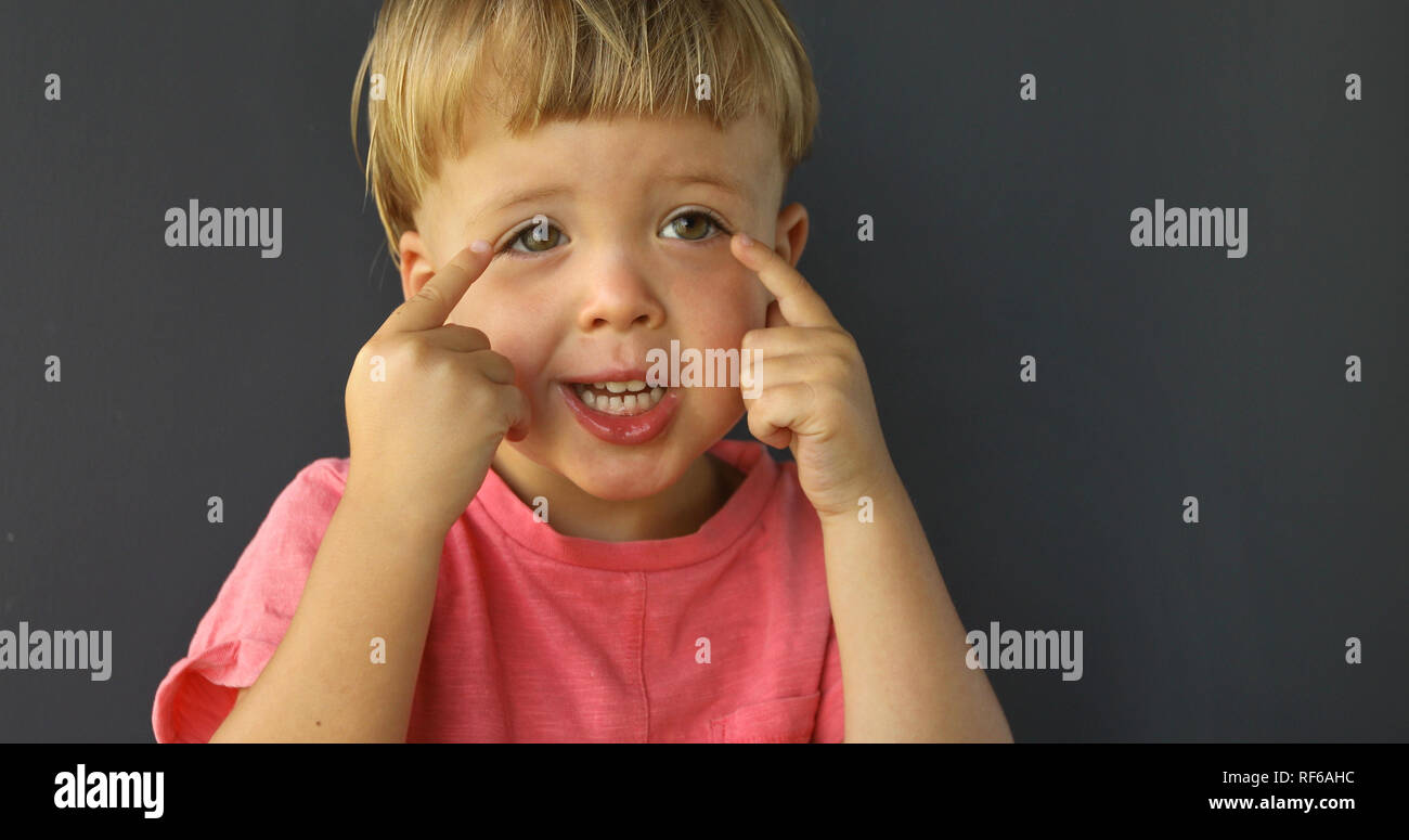 Boy points his fingers of both hands on his eyes Stock Photo
