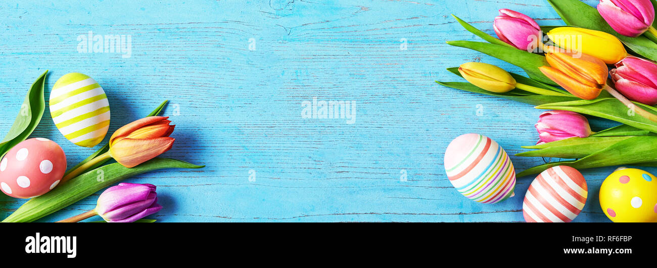 Pretty turquoise blue Easter banner with colorful fresh spring tulips and scattered patterned Easter eggs and copy space for a holiday greeting or hea Stock Photo