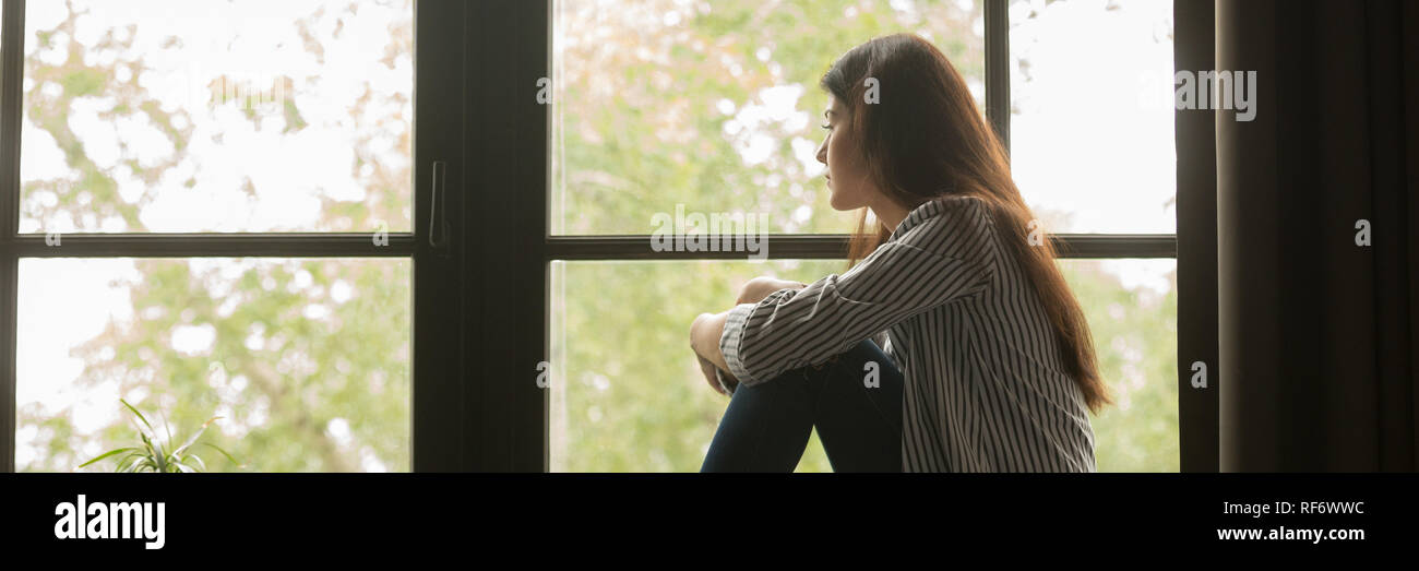 Sad young woman sitting looking out window and thinking Stock Photo - Alamy