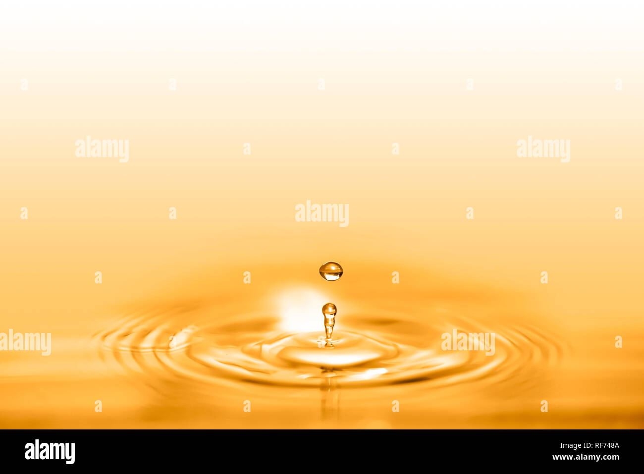 Closeup on drop of cosmetic golden oil liquid creating a circular wave. Stock Photo